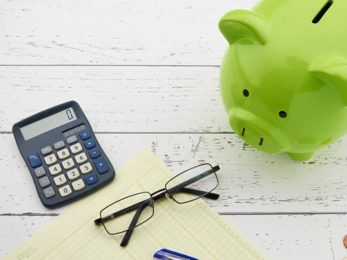 A calculator, notepad and money box laid out on a desk