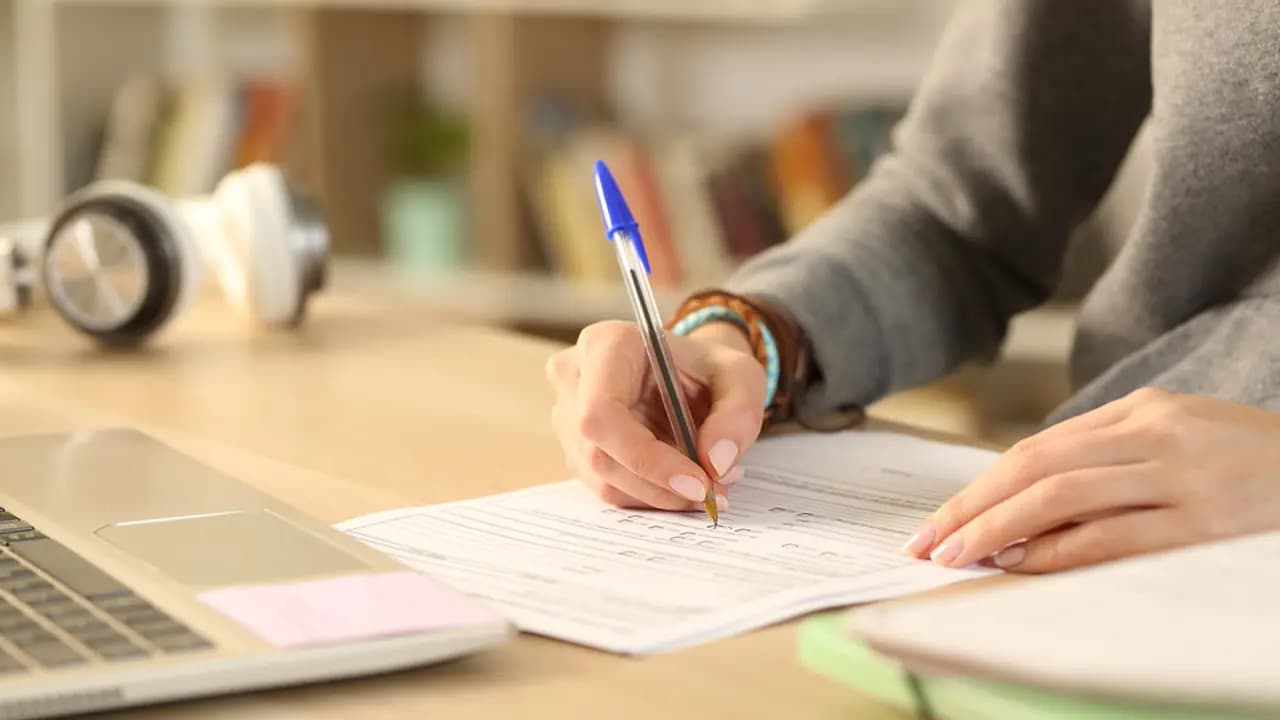 A hand filling in a paper form beside a laptop