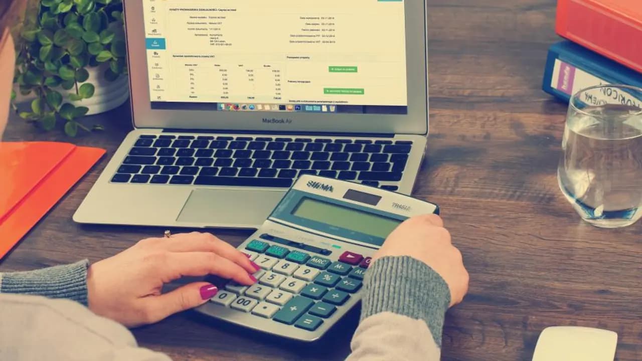 Hands working a calculator beside a laptop of figures